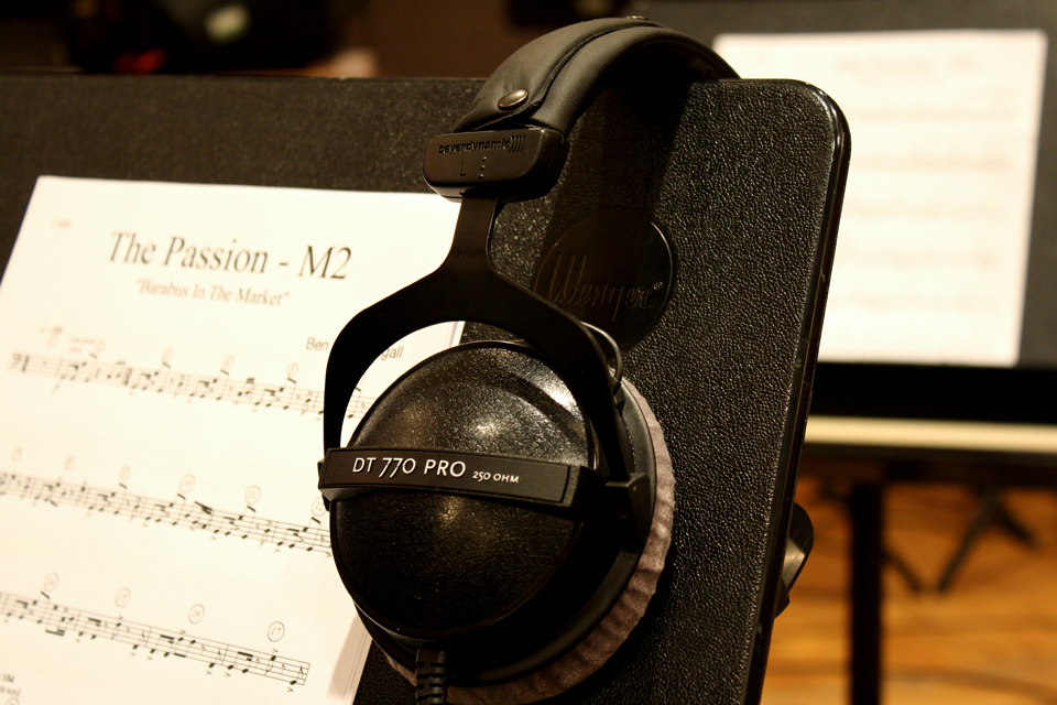 Black headphones and music sheets on a music stand, with a wooden background in the background.